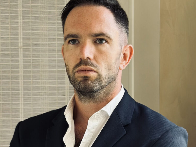 Headshot of a young man indoors wearing a suit, with a serious expression