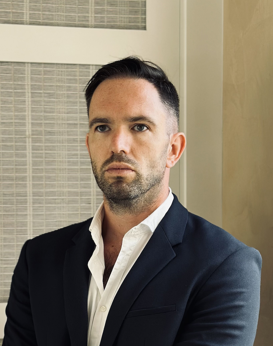 Headshot of a young man indoors wearing a suit, with a serious expression