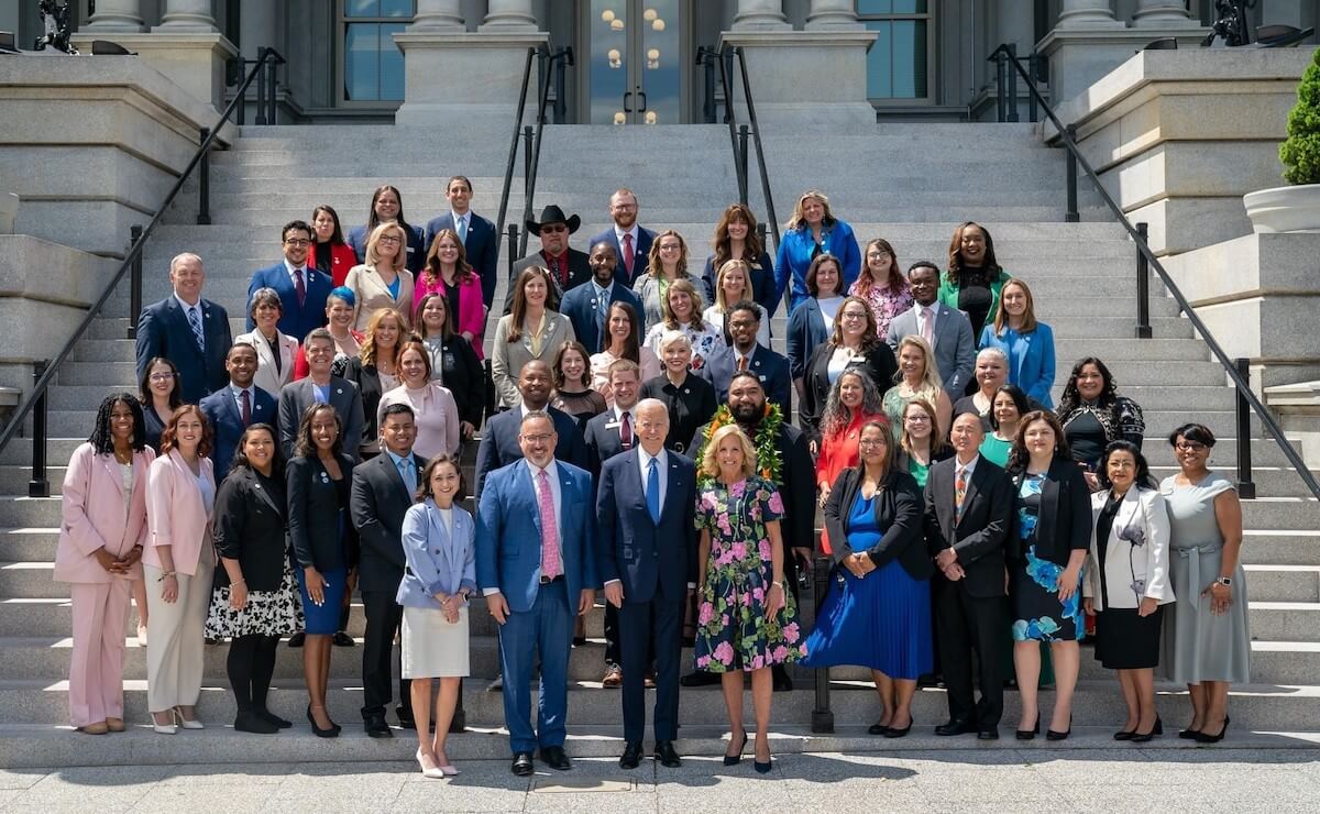 Group of adults standing at the steps to the White House with President Joe Biden and First Lady Jill Biden, formally dressed and smiling