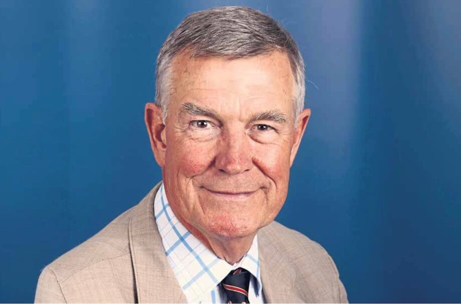 Headshot of a man wearing a checkered shirt and tie, smiling, against a blue background