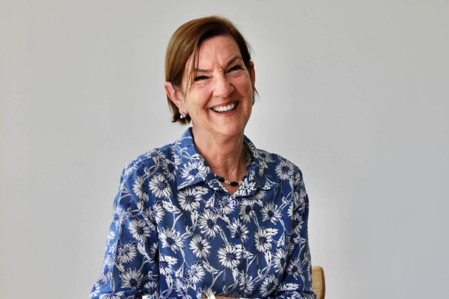 A woman sitting at a table, smiling and wearing a blue flower-covered blouse