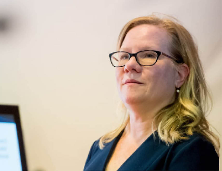 Headshot of a woman wearing glasses and a blazer, working at a computer