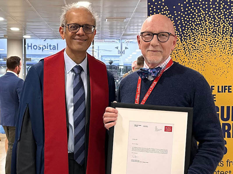 Two men in glasses smiling at King's College London's graduation ceremony, one wearing graduation robes