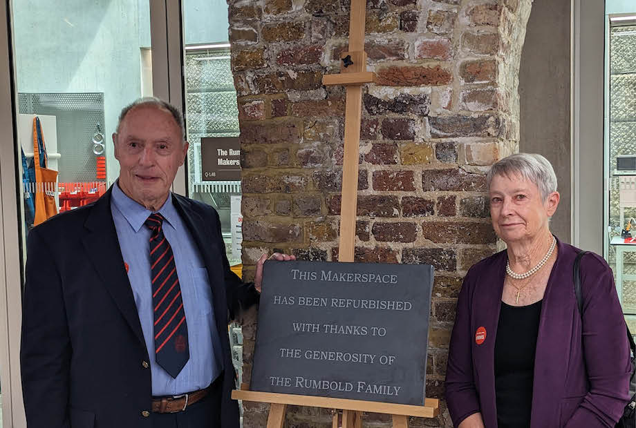 An older man and woman standing at the entrance to the Rumbold Makerspace lab, next to a sign.