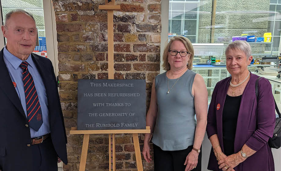 A man and two women, formally dressed, standing at the entrance to the Rumbold Makerspace lab, next to a sign.